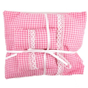 May include: A pink and white gingham doll bed set with a white ribbon tied around it. The set includes a pillow, a blanket, and a fitted sheet.