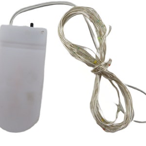 Könnte beinhalten: Ein weißer Batteriepack mit einem Kabel, das an eine Lichterkette mit mehrfarbigen LED-Lichtern befestigt ist. Die Lichter sind weiß, rot, gelb und grün.