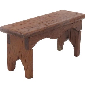 Könnte beinhalten: Eine kleine Holzbank mit schlichtem Design. Die Bank ist aus braunem Holz gefertigt und hat eine rechteckige Oberseite und vier Beine. Die Beine sind leicht gebogen und haben ein schlichtes Design.