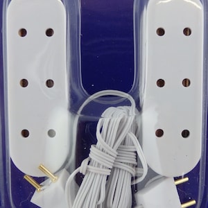 May include: Two white plastic electrical outlet covers with three holes each, packaged with a white electrical cord with a plug on each end.
