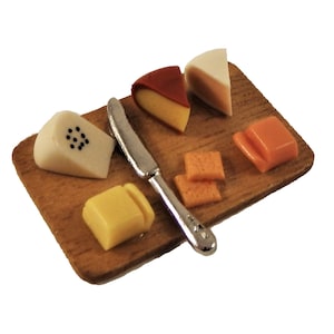 Puede incluir: Una tabla de cortar de madera con una variedad de quesos, incluyendo cheddar, brie y un queso con granos de pimienta negra. También hay un cuchillo de mantequilla plateado en la tabla.