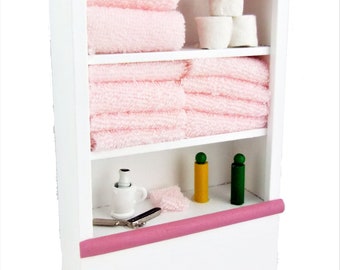 May include: White wooden shelf unit with three shelves, featuring pink towels, white cotton balls, and small bottles. The shelf has a pink trim.