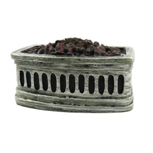 May include: A small, rectangular decorative fireplace with a weathered, grey-green finish. The front has vertical oval cutouts. The top is filled with dark brown, textured material, resembling coals. A miniature home decor item.