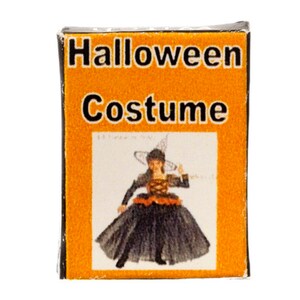 May include: A box with an orange background and black text that reads "Halloween Costume". The box features a picture of a girl dressed as a witch wearing a black dress and a pointed hat.