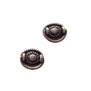 May include: Two antique bronze drawer pulls with an oval center and decorative detailing. Each pull has a small handle on either side of the oval. The pulls are set against a white background.