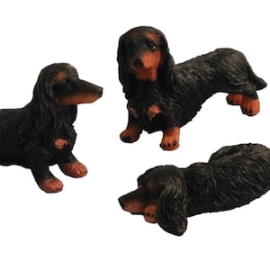 Könnte beinhalten: Drei schwarze Dackelfiguren, eine sitzend, eine stehend und eine liegend. Die Figuren sind aus glattem, bemaltem Material gefertigt und haben realistische Details.