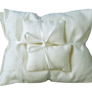 May include: A white pillow with lace trim and a satin ribbon tied around it. The pillow is made of soft fabric and is ideal for holding rings or other small items.