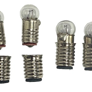 May include: A collection of small, clear glass light bulbs with silver-colored metal bases. The bulbs have a rounded shape and a visible filament inside. Several bases are also shown, some with a red or black base.