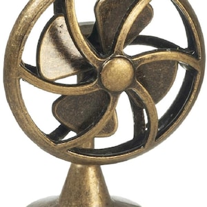 Puede incluir: Un mini ventilador de metal dorado con una base redonda y una hélice de cinco aspas. El ventilador es un objeto decorativo.