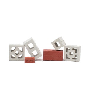 Puede incluir: Un conjunto de bloques de hormigón en miniatura en blanco y rojo. El conjunto incluye cuatro bloques con diferentes diseños y un pequeño ladrillo.