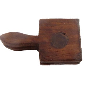 May include: A wooden tool with a square head and a handle shaped like a rounded spoon. The head has a circular hole in the centre.