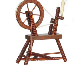 May include: A miniature wooden spinning wheel with a dark brown finish. The wheel has a circular design with spokes and is connected to a frame with turned legs. White yarn is wrapped around the wheel and spindle, with an orange string connecting the wheel to the base.