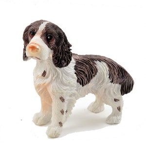 May include: A figurine of a Springer Spaniel dog, featuring a brown and white coat. The dog is in a standing pose, with detailed fur texture and realistic features. The figurine has a white background.