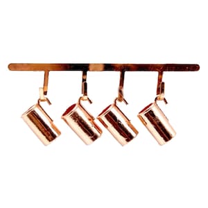 May include: Four copper mugs hang from a metal rack. The mugs are all the same size and shape, and they have a shiny, metallic finish.