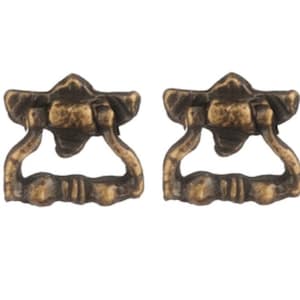 Könnte beinhalten: Zwei antike Messing-Schubladengriffe mit dekorativem Design. Die Griffe haben eine Ringform mit einem dekorativen Ober- und Unterteil.