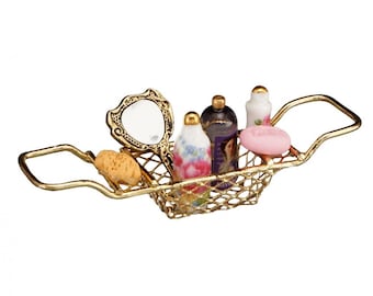 Puede incluir: Una cesta de alambre dorada con asas que contiene un pequeño espejo de mano, una pastilla de jabón y cuatro frascos en miniatura de artículos de tocador. Los frascos están decorados con motivos florales y uno de ellos tiene el rostro de una mujer.
