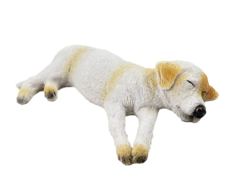 以下が含まれることがあります： 白と茶色の寝ている犬の置物。犬は横向きに寝ていて、頭は前足の上に置かれています。置物は滑らかでリアルな素材で作られています。