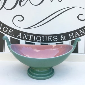 Könnte beinhalten: Eine grüne und rosafarbene Keramikschale mit zwei Griffen. Die Schale steht auf einem Sockel und hat eine glänzende Oberfläche.