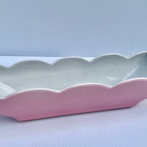 Könnte beinhalten: Eine rosa und weiße Keramik-Servierplatte mit einem gewellten Rand. Die Platte ist lang und schmal und hat eine glatte, glänzende Oberfläche.