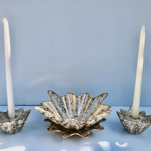 May include: A vintage candle holder set and decorative bowl. The candle holders and bowl are white with gold and black speckled accents. Two white candles are in the candle holders. The bowl is star-shaped.