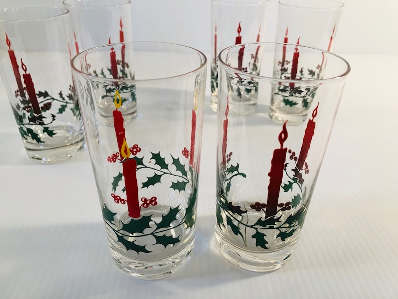 Peut inclure: Ensemble de verres &agrave; boire transparents avec un motif de bougie de No&euml;l. Chaque verre pr&eacute;sente une bougie rouge avec une flamme jaune, du houx et des baies. Parfait pour les f&ecirc;tes de fin d'ann&eacute;e.