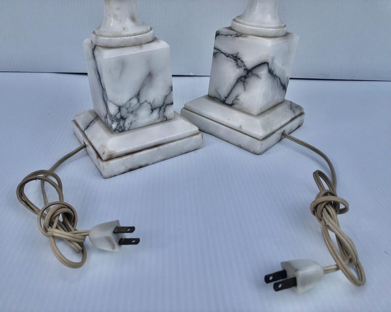 Puede incluir: Dos l&aacute;mparas de m&aacute;rmol a juego con un patr&oacute;n veteado blanco y gris. Cada l&aacute;mpara tiene una base cuadrada y una parte superior cil&iacute;ndrica. Las l&aacute;mparas est&aacute;n conectadas a cables el&eacute;ctricos con enchufes de dos clavijas.