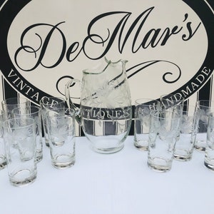 May include: A set of 10 clear glass tumblers and a jug with an etched floral design. The glasses and jug are arranged on a white surface. The background is a black and white striped pattern with the text "DeMar's Vintage Antiques Handmade".