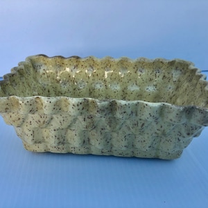 May include: A yellow ceramic planter with a speckled brown glaze and a wavy, textured rim.