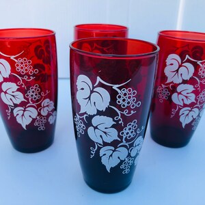 Könnte beinhalten: Vier rote Glasbecher mit einem weißen Weinreben-Design. Die Gläser sind klar und haben einen Vintage-Look.