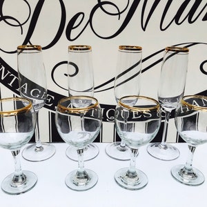 Peut inclure: Ensemble de huit verres à vin en verre transparent avec des bords dorés. Les verres sont disposés en deux rangées de quatre. Les verres sont tous vides.