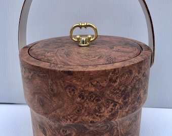 May include: A brown faux wood ice bucket with a gold handle and lid. The bucket has a wood grain pattern.
