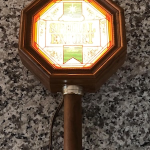 May include: A vintage beer tap handle with a wooden shaft and a decorative top. The top features an octagonal design with the words "SPECIAL EXPORT" illuminated in a stained-glass style. The handle has brass accents and a gold-colored finial.