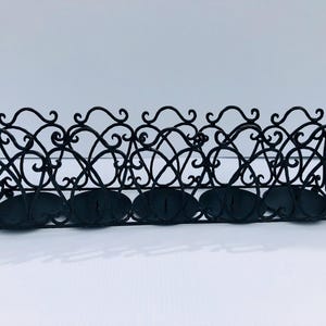 Puede incluir: Candelero de metal negro con un diseño decorativo de desplazamiento. Tiene cuatro portavelas separados.