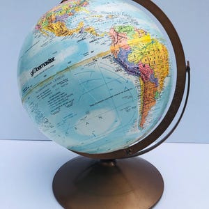 May include: A vintage globe with a bronze base and meridian ring. The globe displays a detailed map with countries in various colours, including blue oceans and continents in shades of yellow, green, and brown. The text "Globemaster Legend" is visible on the globe.