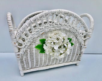 Vintage weißes Weiden-Magazin-/Buch-/Aufbewahrungsregal mit weißen Blumen und grünen Blättern auf beiden Seiten des Korbs, Cottage, French Decor