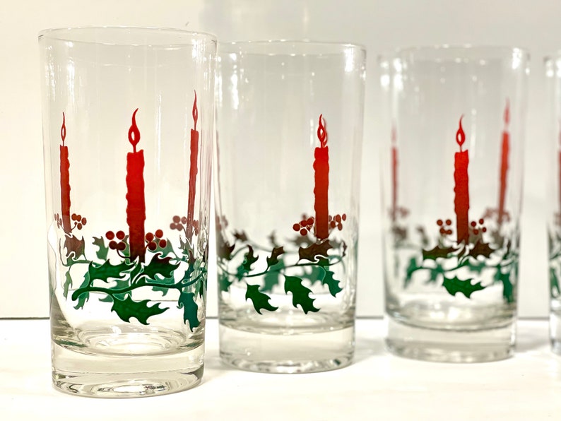 Peut inclure: Ensemble de verres transparents avec un motif de bougie de No&euml;l. Chaque verre pr&eacute;sente une longue bougie rouge avec une flamme, des feuilles de houx vertes et des baies rouges. Id&eacute;al pour les boissons de f&ecirc;te.