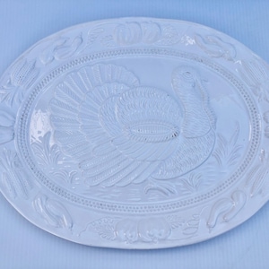 Puede incluir: Plato de servir ovalado de cerámica blanca con un diseño en relieve de un pavo. El plato tiene un borde elevado y un borde decorativo.