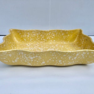 May include: A yellow ceramic serving dish with a white speckled glaze. The dish has a wavy edge and is rectangular in shape.