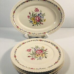 Pode incluir: Conjunto de quatro pratos de jantar de cerâmica branca com um design floral. Os pratos têm uma borda festonada e um delicado padrão floral em tons de rosa, amarelo e azul.