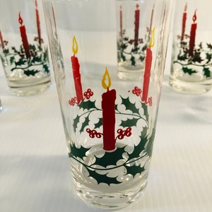 Peut inclure: Verres &agrave; boire transparents avec un motif de No&euml;l festif. Chaque verre pr&eacute;sente une bougie rouge avec une flamme jaune, entour&eacute;e de feuilles de houx vertes et de baies rouges. Les verres sont cylindriques et semblent &ecirc;tre en verre.