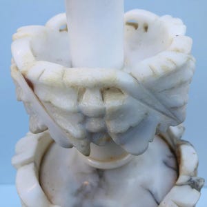Puede incluir: Un par de candelabros de m&aacute;rmol blanco. Los candelabros presentan intrincadas tallas de hojas y flores. El m&aacute;rmol tiene un aspecto veteado natural con sutiles variaciones de color, lo que se suma a su est&eacute;tica antigua.