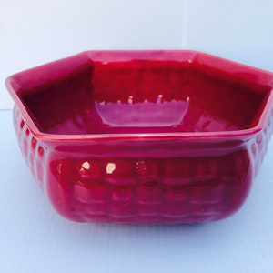 Puede incluir: Un cuenco hexagonal de cerámica rojo oscuro con un patrón tejido texturizado. El cuenco está vacío y listo para ser llenado.