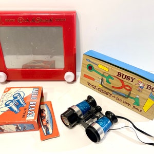 May include: A red Etch A Sketch toy, a blue and brown tool chest labeled "Busy Boy Tool Chest with Safe Vinyl Tools", a box of field glasses, and a pair of blue binoculars with a black strap.