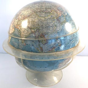 May include: A vintage globe with a clear plastic casing and base. The globe features a detailed map of the world with countries and oceans in various colors. The globe is a decorative educational item.