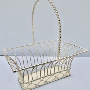 Può includere: Cestino in metallo bianco sporco con forma rettangolare e manico intrecciato. Il cestino presenta un design traforato con linee arcuate e curve. La base ha un motivo decorativo a croce. Il cestino è adatto a vari scopi decorativi o di stoccaggio.