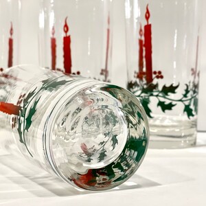 Peut inclure: Verres &agrave; boire transparents avec un motif de bougie de No&euml;l festif. Chaque verre pr&eacute;sente une bougie rouge avec une flamme vacillante, des feuilles de houx vertes et des baies rouges. Id&eacute;al pour les boissons de f&ecirc;te.