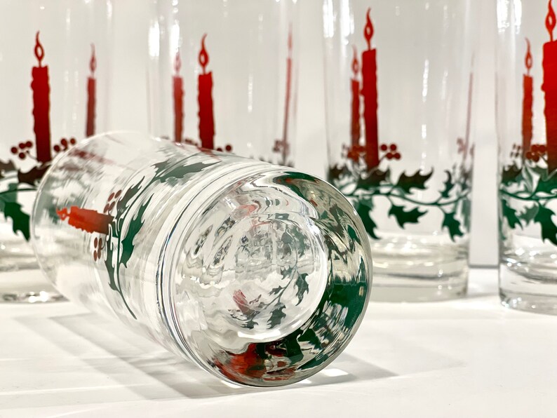 Peut inclure: Verres &agrave; boire transparents avec un motif de bougie de No&euml;l festif. Chaque verre pr&eacute;sente une bougie rouge avec une flamme vacillante, des feuilles de houx vertes et des baies rouges. Id&eacute;al pour les boissons de f&ecirc;te.