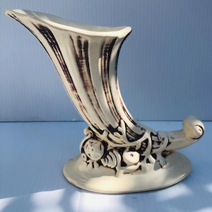May include: Cream ceramic cornucopia vase with brown vertical stripes and decorative base. The vase has a curved, horn-like shape. Likely vintage or antique, it is a decorative item.