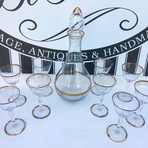 Peut inclure: Un ensemble de neuf carafes et verres en verre transparent avec des finitions dorées. La carafe a un long col fin et un corps rond. Les verres sont petits et ont un large bol. L'ensemble est parfait pour servir du vin ou d'autres boissons.