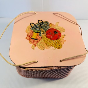 Peut inclure: Un panier de couture rose vintage avec une base tissée et un couvercle orné d'une tomate, de ciseaux et d'une bobine de fil. Le panier est doté d'une poignée et est conçu pour ranger les fournitures de couture. Le design général est de style rétro.